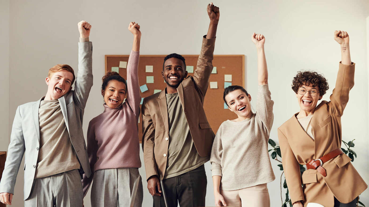 5 junge Kollegen stehen im Büro und reizen vor Freude die Arme in die Luft